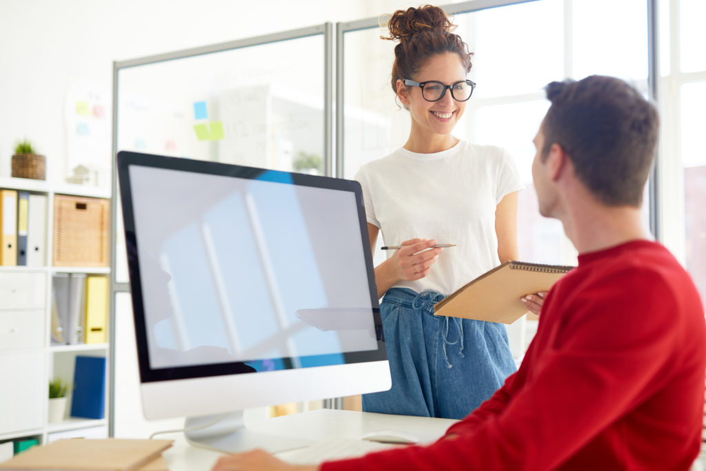 Woman and man discussing security insights and lifestyle trends near computer monitor.