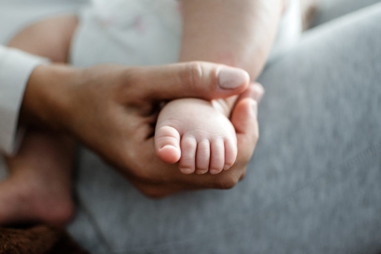 Newborn baby's foot held in adult hand, illustrating health and well-being for home design.