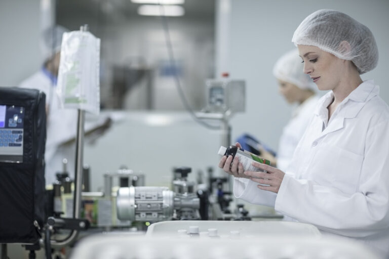 Woman in pharmaceutical plant examining a flask, quality control and safety procedures.