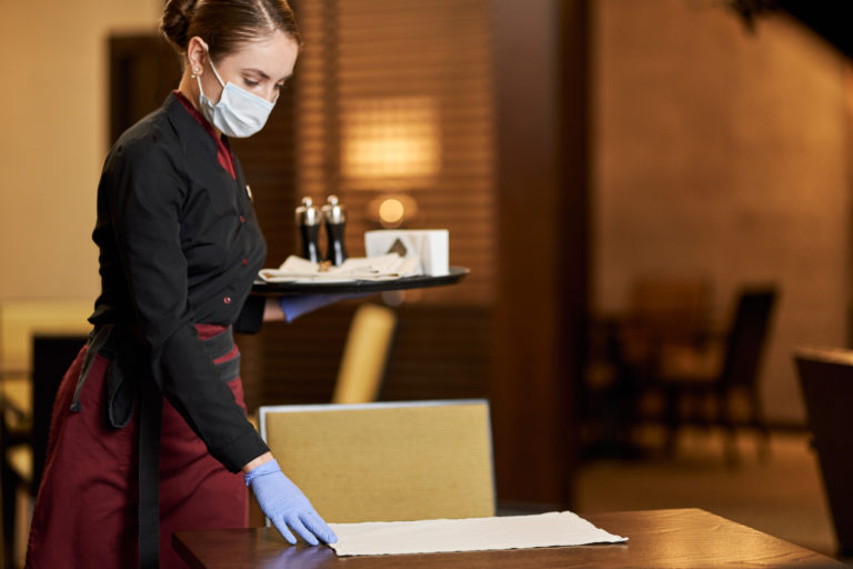 Restaurant staff member with mask and gloves serving food, illustrating safe practices for Florida celebrations.