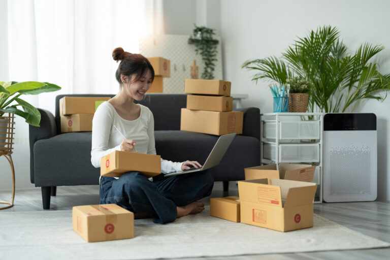 Small business owner using laptop surrounded by shipping boxes and packages.